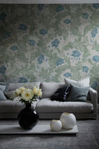 Poppy wallpaper by Sandberg in sage green with blue poppies, styled in a living room behind a grey sofa and round vases