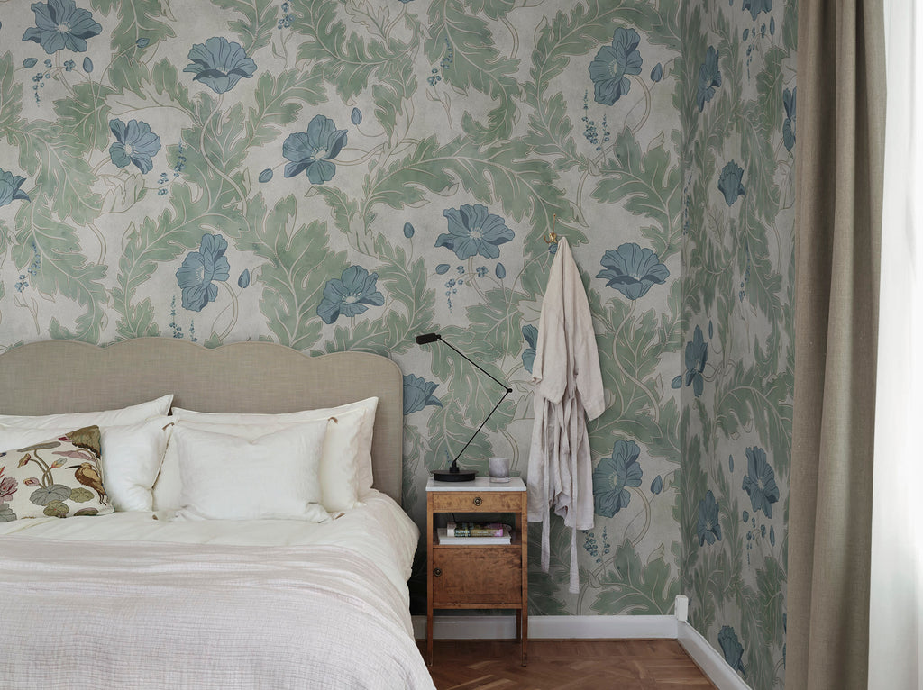 Poppy wallpaper by Sandberg in sage green with blue poppies, styled in a bedroom behind a linen headboard and timber side table