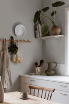 Einar wallpaper by Sandberg in pale grey on a kitchen wall styled with hanging apron, peg rail and shelf