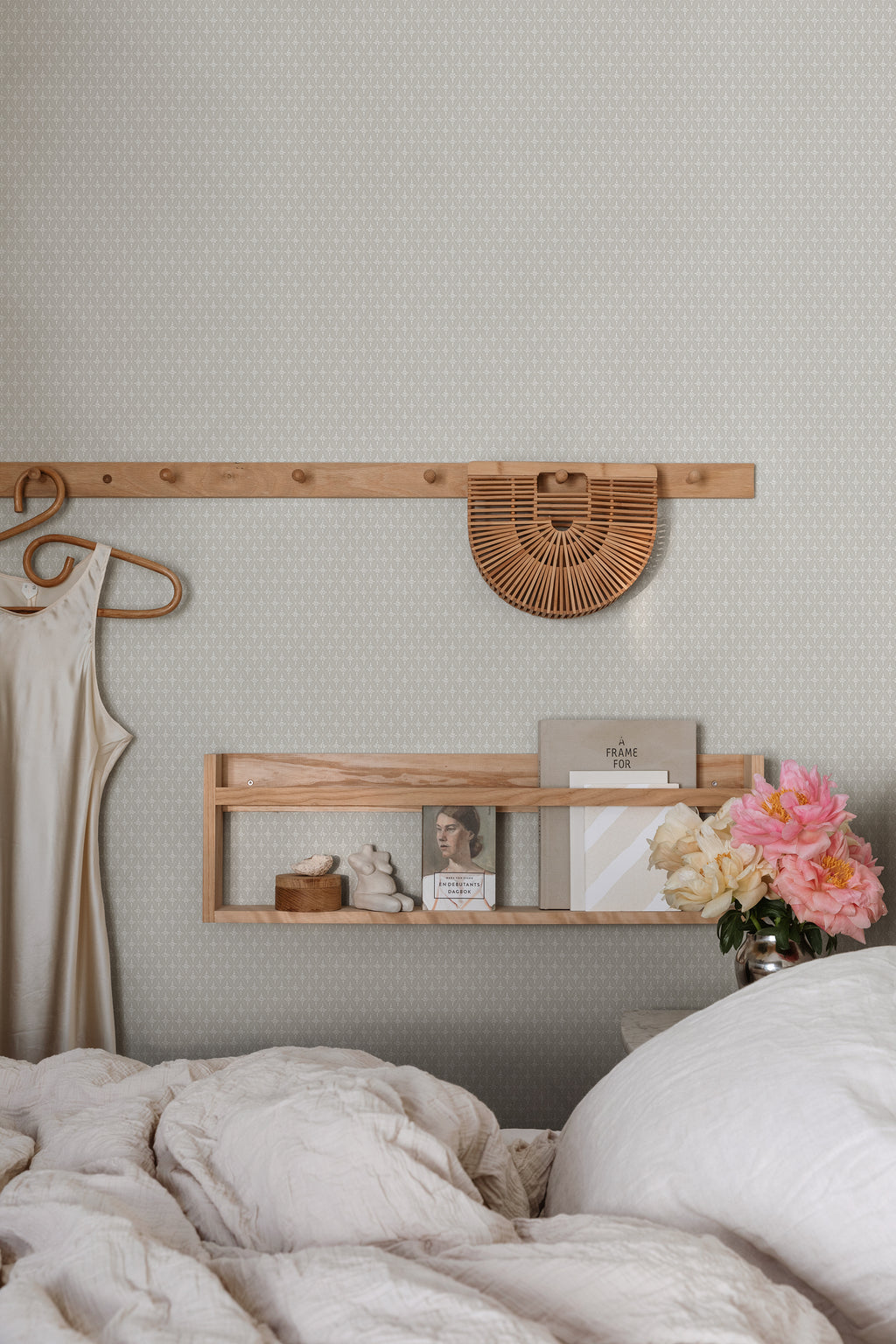 Einar wallpaper by Sandberg in light grey behind a bed with linen bedding and a peg rail