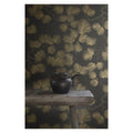 Pine wallpaper by Sandberg in gold on dark charcoal styled behind a rustic bench with a black teapot