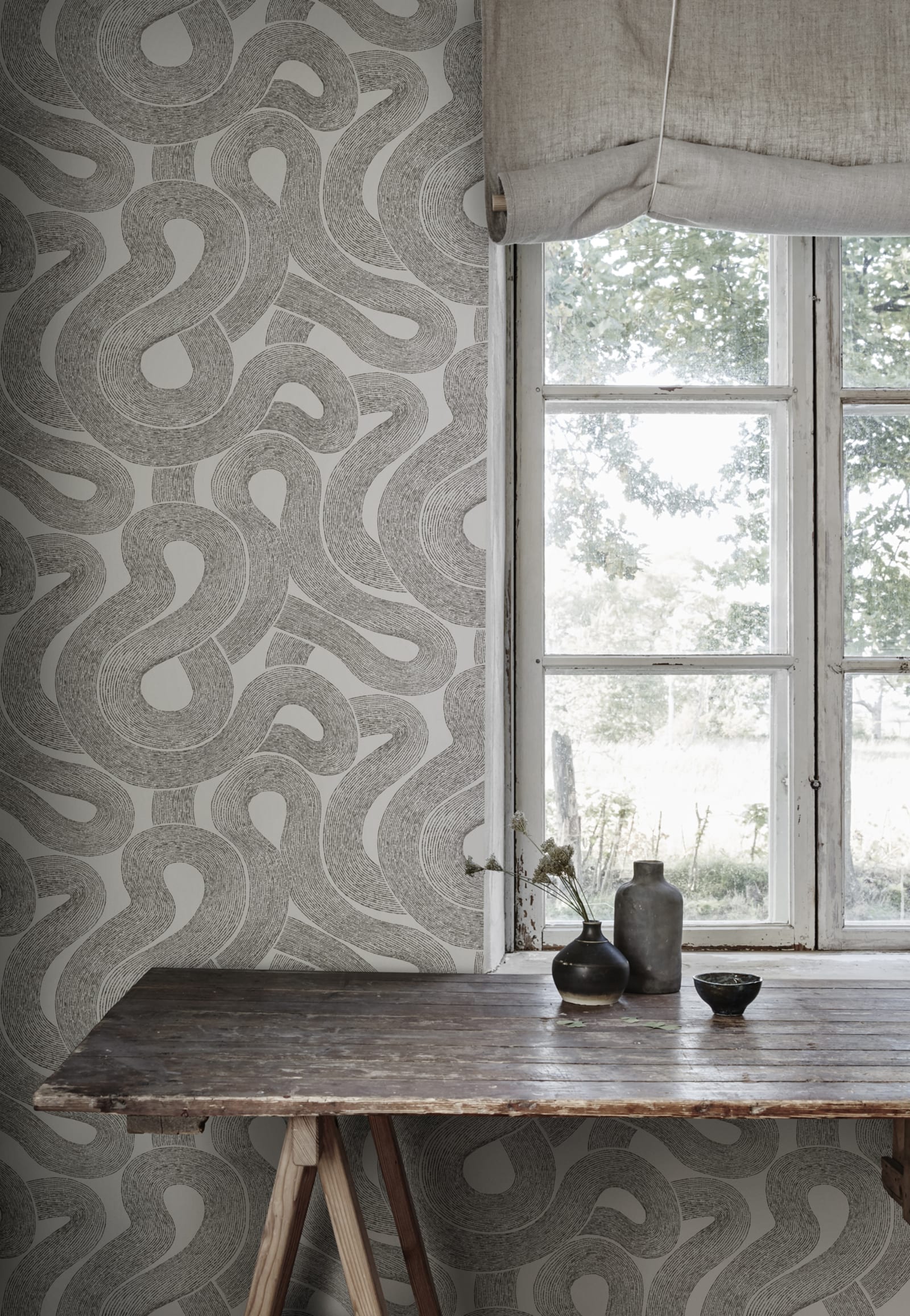 Zen wallpaper by Sandberg in charcoal looping print beside a rustic trestle table by a cottage window