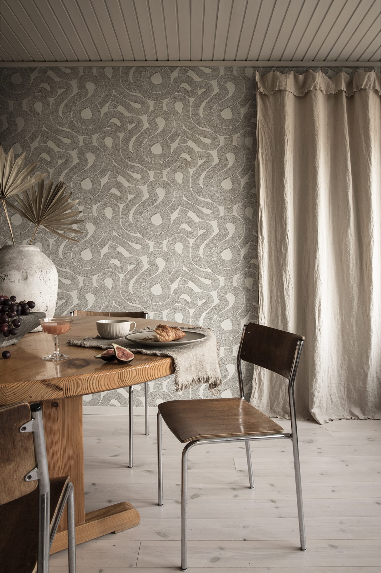 Zen wallpaper by Sandberg in charcoal looping print in a dining nook with a wooden table and linen curtain