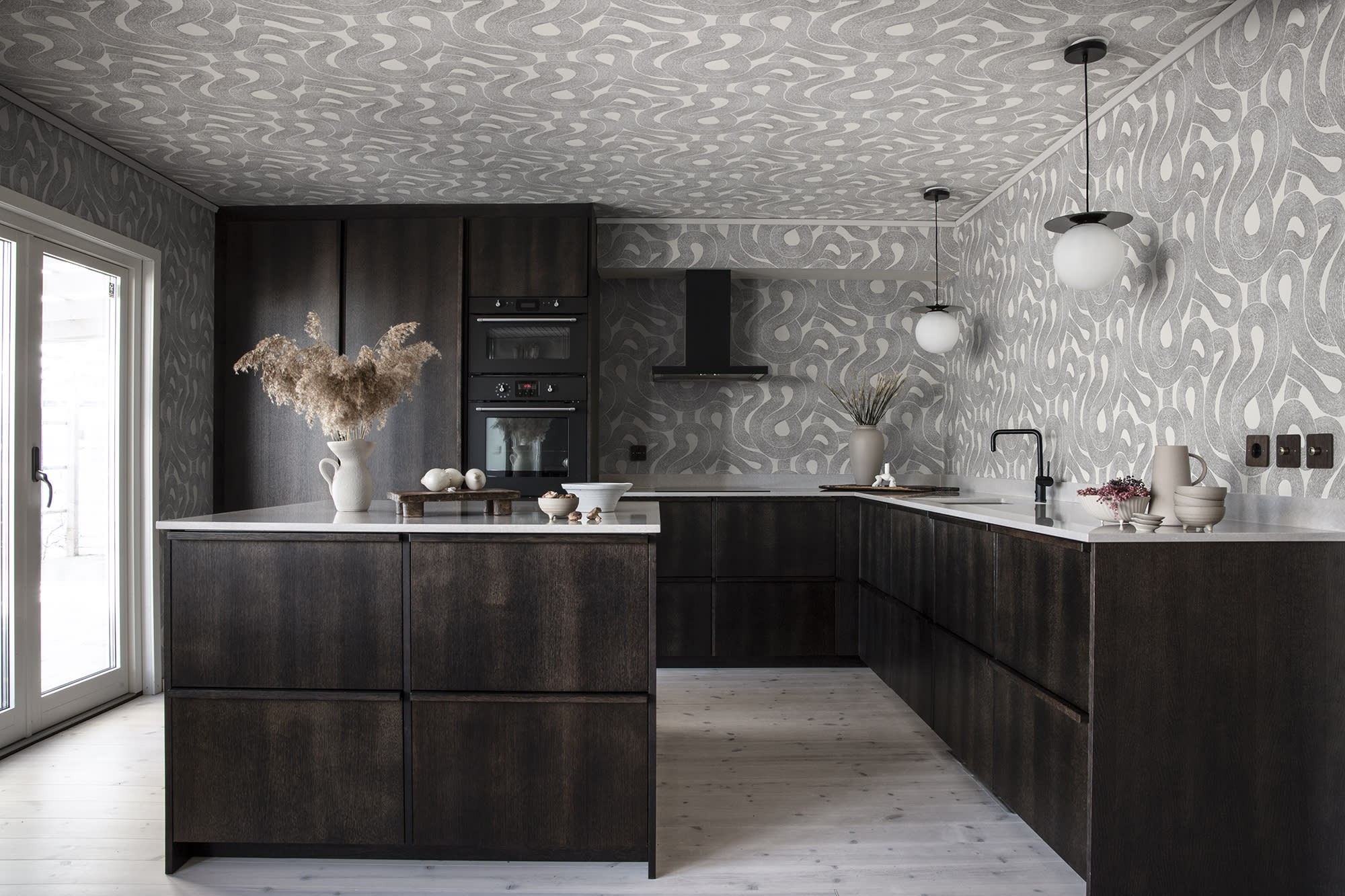 Zen wallpaper by Sandberg in charcoal looping print across the walls and ceiling of a dark timber kitchen