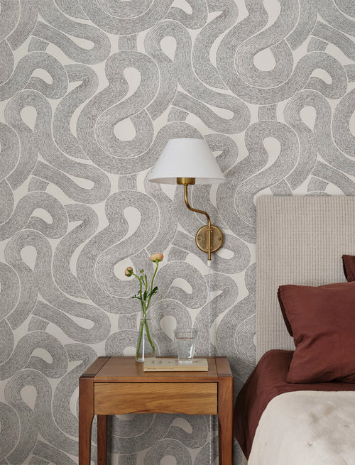 Zen wallpaper by Sandberg, swirling looped line pattern in charcoal on white behind a bedside table and brass lamp