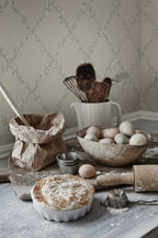 Ewa wallpaper by Sandberg in pale sage trellis floral behind a rustic baking still life with eggs and pie