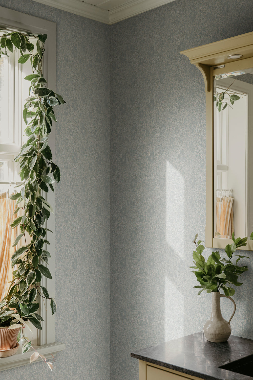 Anton wallpaper by Sandberg in pale grey in a corner with a trailing plant, window and yellow mirror