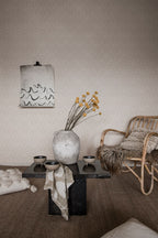 Emil wallpaper by Sandberg in pale greige in a living room with rattan chair, stone vase and low table