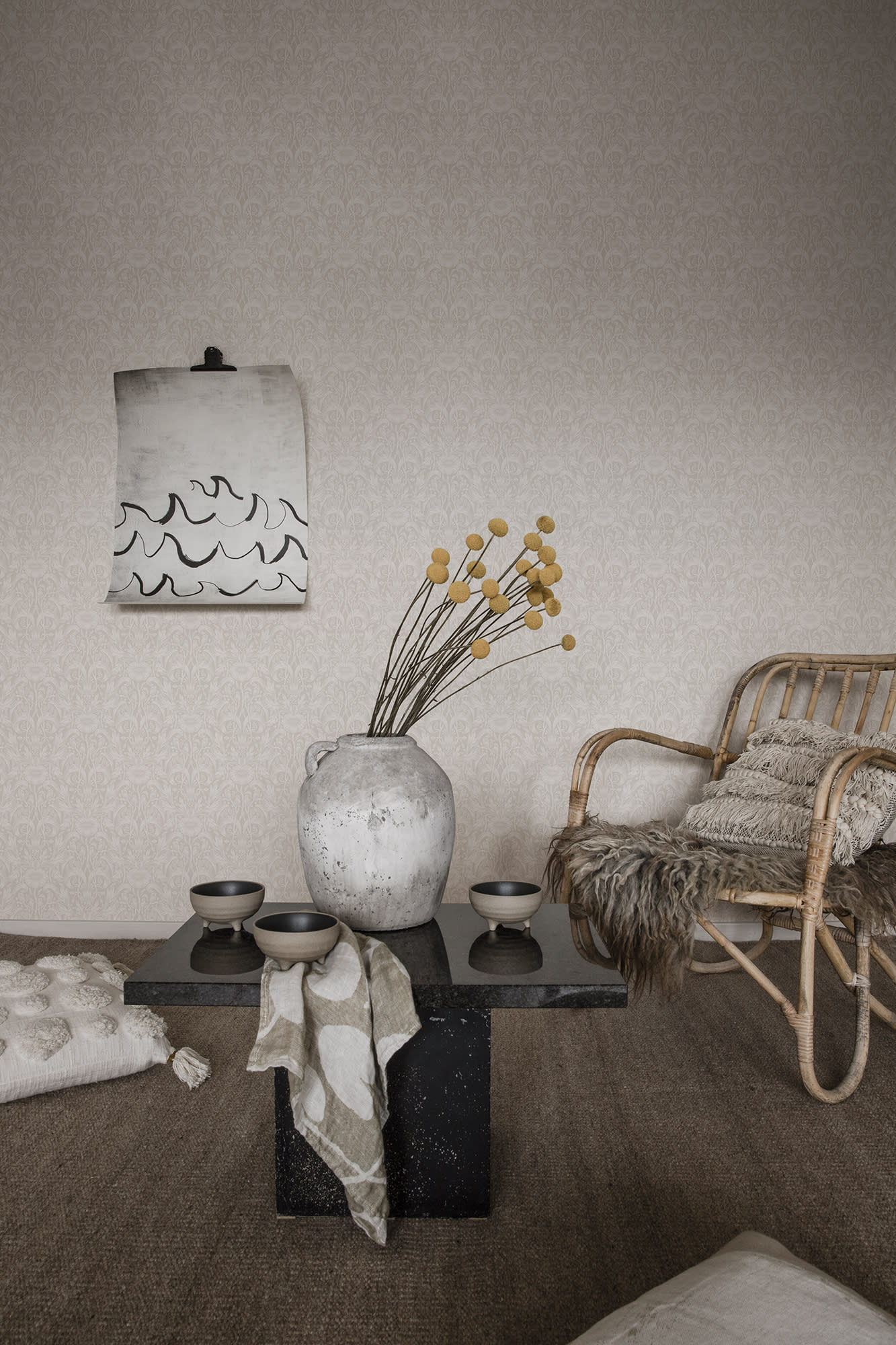 Emil wallpaper by Sandberg in pale greige in a living room with rattan chair, stone vase and low table