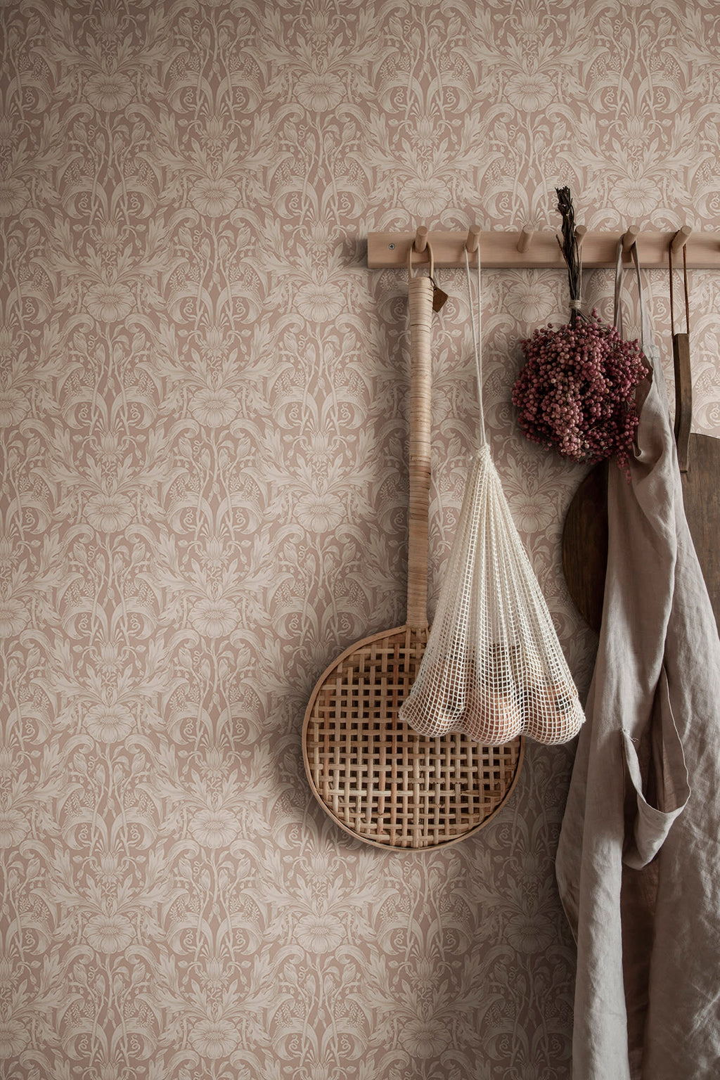 Emil wallpaper by Sandberg in dusty pink on a wall with peg rail holding a net bag and linen apron