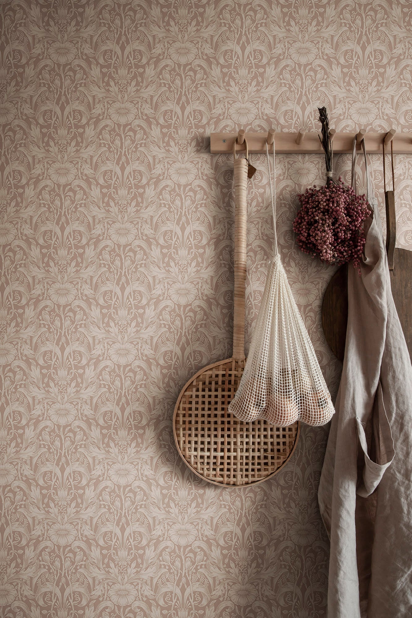 Emil wallpaper by Sandberg in dusty pink on a wall with peg rail holding a net bag and linen apron