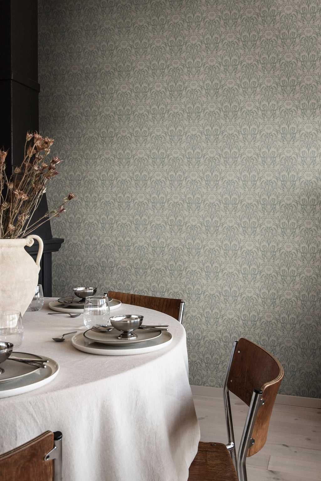 Emil wallpaper by Sandberg in sage green behind a linen-set dining table with timber chairs