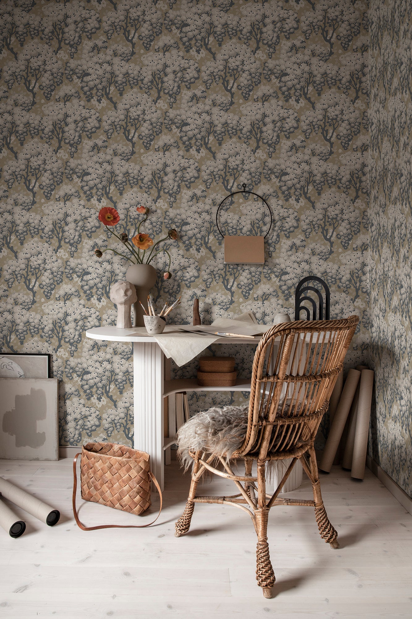 Ragnvi wallpaper by Sandberg in a home studio, blossom tree pattern behind a white desk, rattan chair and vase of poppies