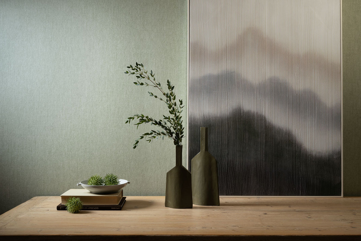 Flamant Terre de Lin wallpaper by Arte in Green – Vert d'Eau behind a timber shelf with a vase and a landscape artwork