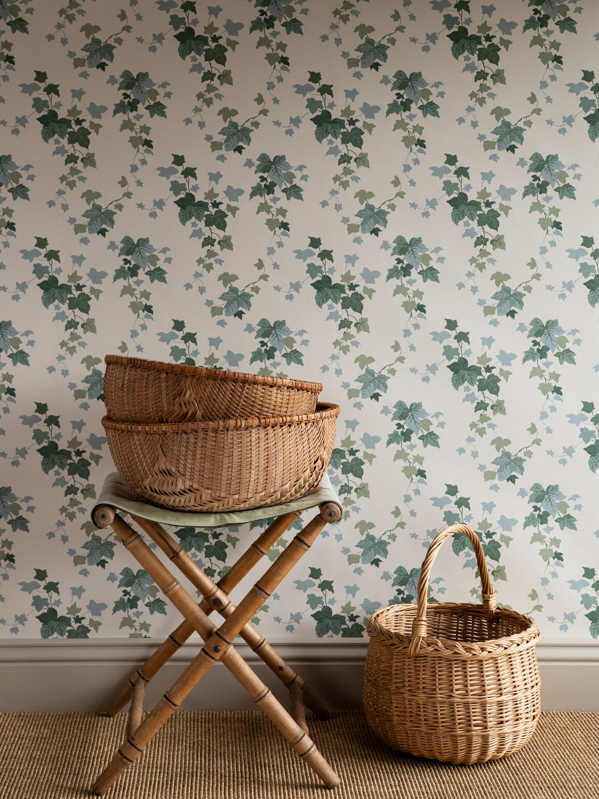 Ivy wallpaper by Långelid/von Brömssen in Green – botanical design, behind a bamboo stool and a wicker basket