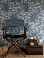Acacia wallpaper by Långelid/von Brömssen in Blue – botanical design, behind a director's chair and wooden boxes