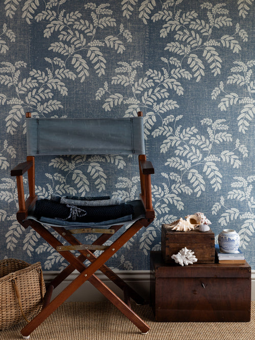 Acacia wallpaper by Långelid/von Brömssen in Blue – botanical design, behind a director's chair and wooden boxes