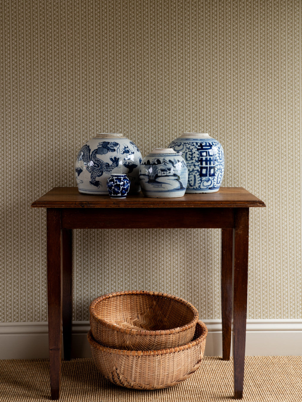 Zigzag wallpaper by Långelid/von Brömssen in Beige – geometric design, behind a wooden table with blue and white ginger jars
