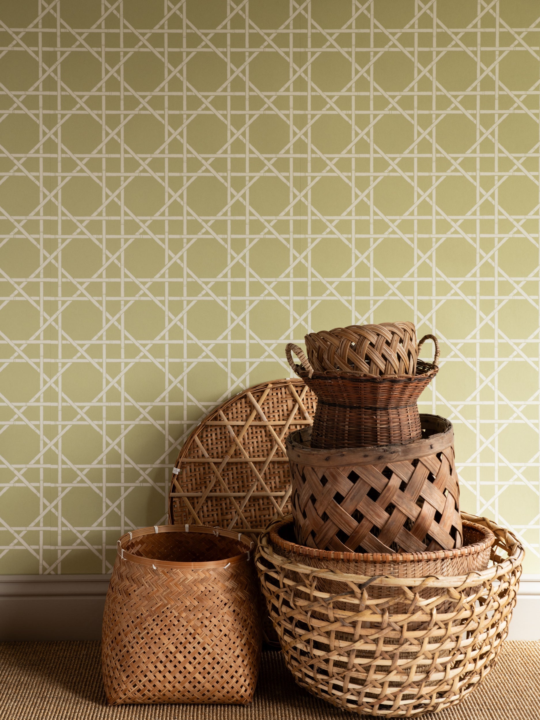 Trellis wallpaper by Långelid/von Brömssen in Green – geometric design, behind a stack of woven baskets