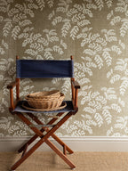 Acacia wallpaper by Långelid/von Brömssen in Beige – botanical design, behind a director's chair with a wicker basket