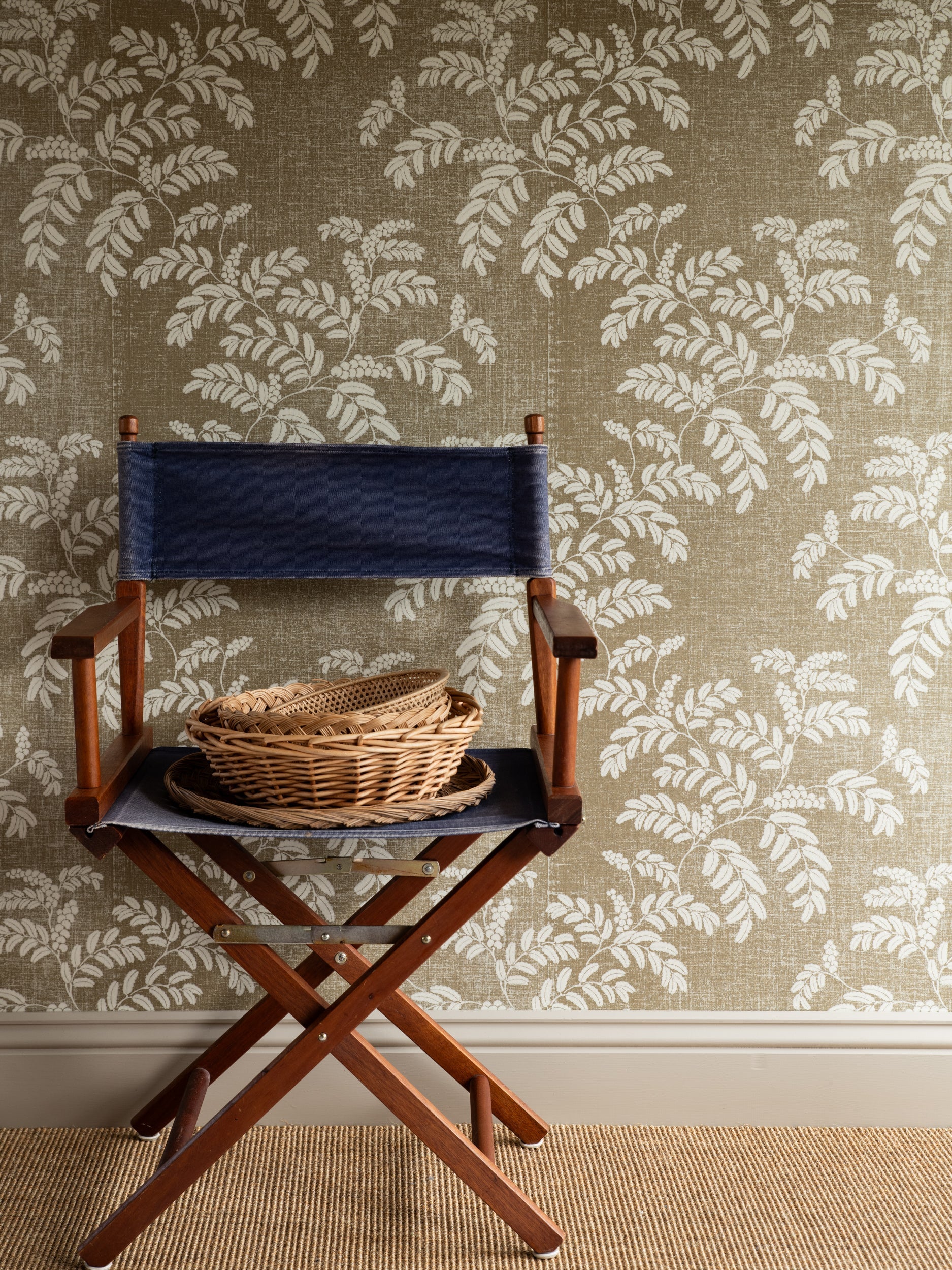 Acacia wallpaper by Långelid/von Brömssen in Beige – botanical design, behind a director's chair with a wicker basket