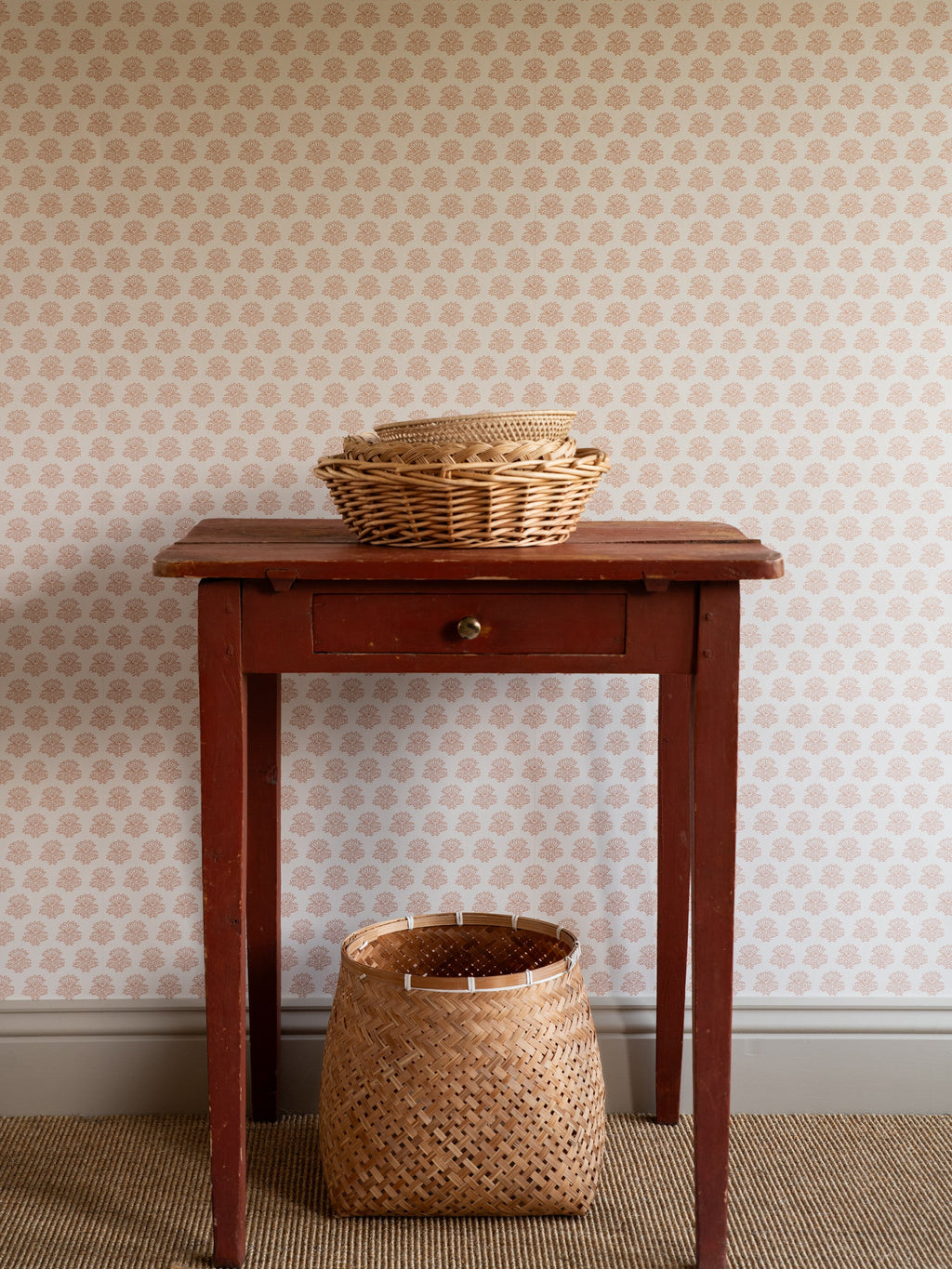 India wallpaper by Långelid/von Brömssen in Peach – floral design, behind a red side table and a wicker basket