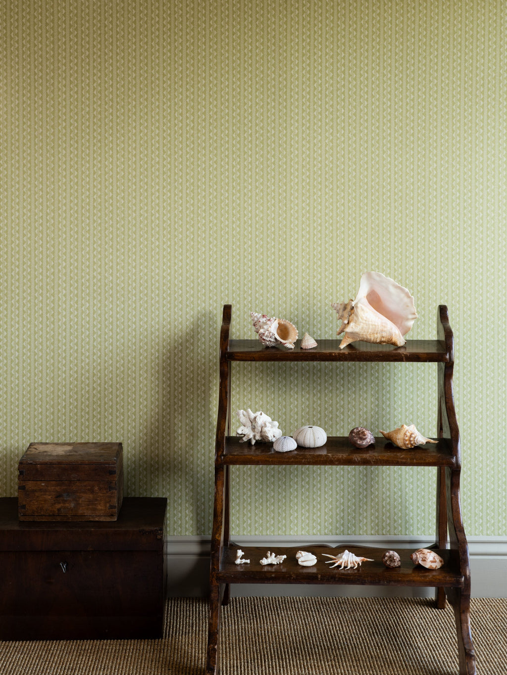 Zigzag wallpaper by Långelid/von Brömssen in Green – Dusty Lemon – geometric design, behind a wooden shelf of shells
