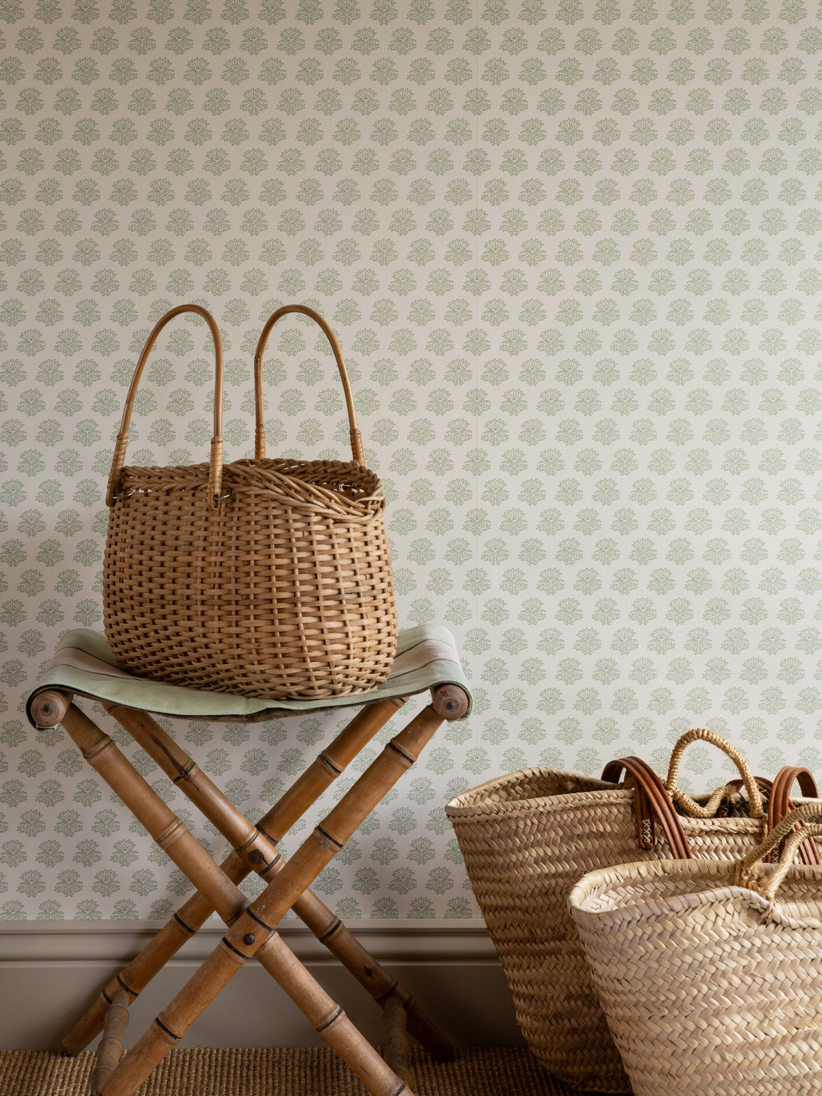 India wallpaper by Långelid/von Brömssen in Sage Green – floral design, behind a bamboo stool and a woven bag