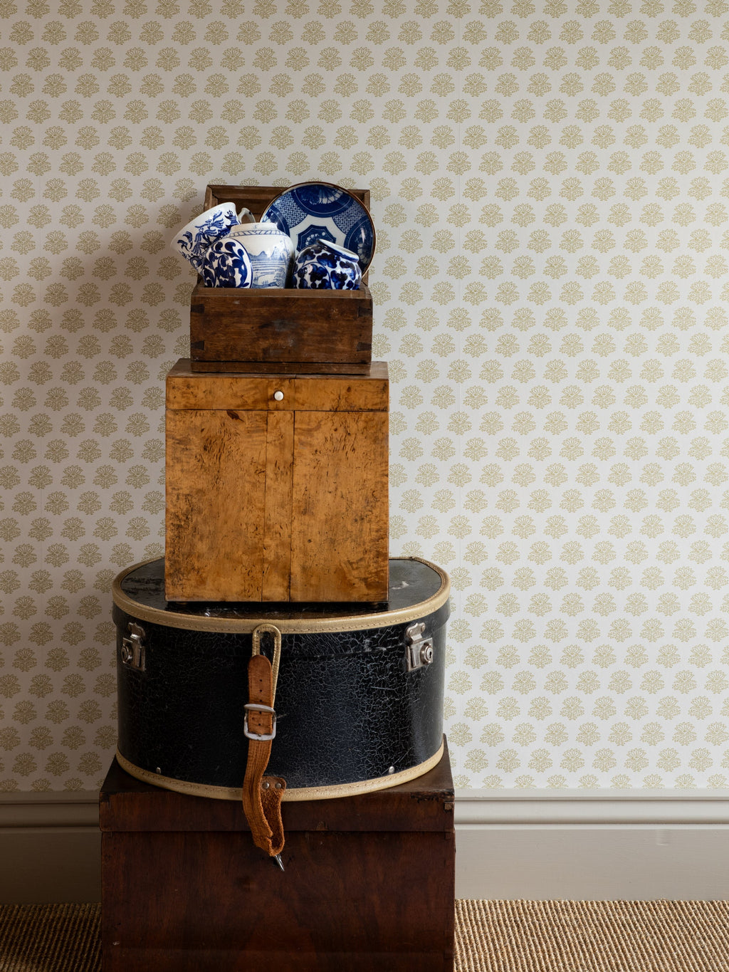 India wallpaper by Långelid/von Brömssen in Yellow – floral design, behind stacked boxes with blue and white china