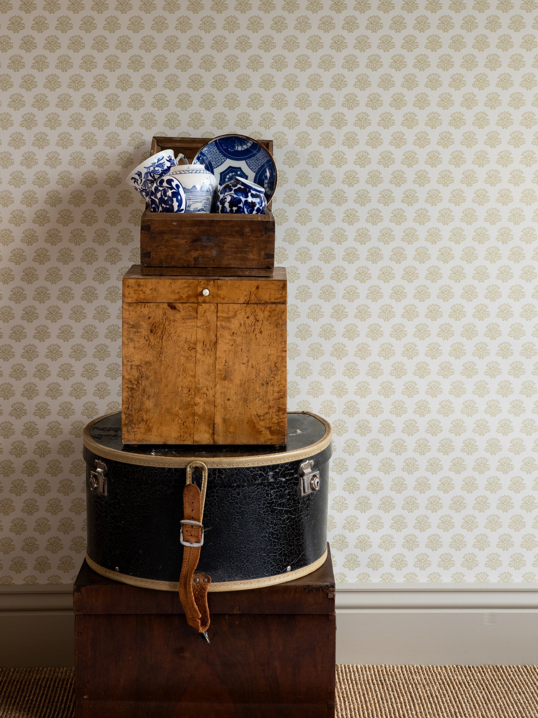 India wallpaper by Långelid/von Brömssen in Yellow – floral design, behind stacked boxes with blue and white china