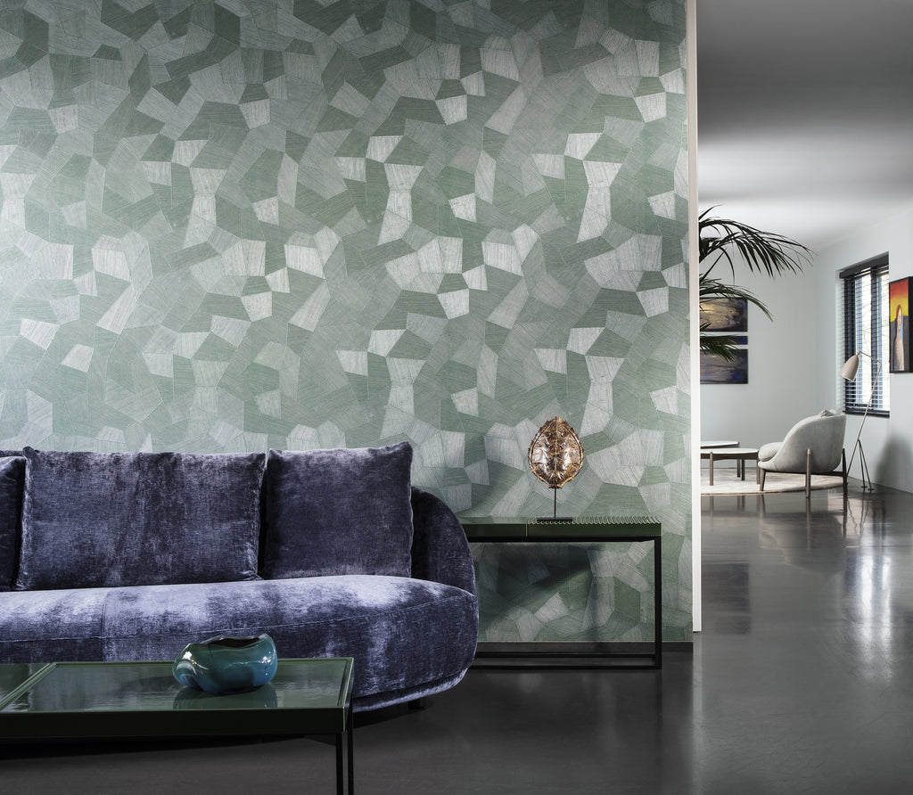 Facet wallpaper by Arte in Green – Eucalyptus behind a purple velvet sofa in an open living space
