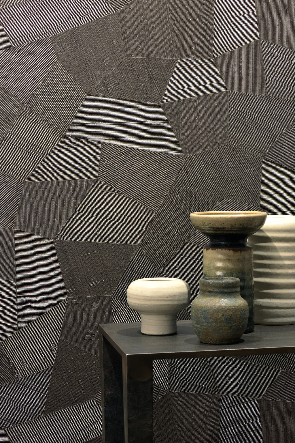Facet wallpaper by Arte in Brown behind a dark side table with ceramic pots and bowls