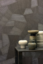 Facet wallpaper by Arte in Brown behind a dark side table with ceramic pots and bowls