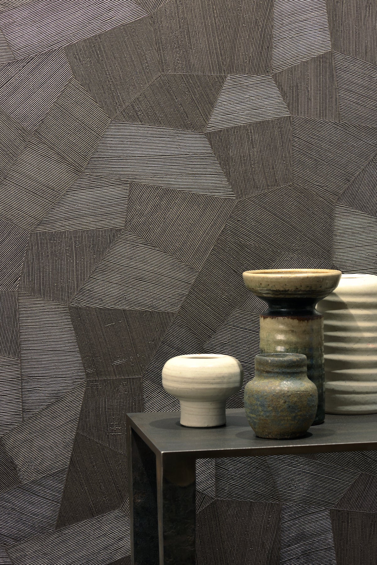 Facet wallpaper by Arte in Brown behind a dark side table with ceramic pots and bowls