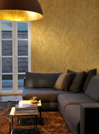 Musa wallpaper by Arte in Gold in a living room with a grey corner sofa, glass doors and a large pendant lamp