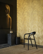 Musa wallpaper by Arte in Gold in an entry with a black chair, stone plinth and a framed portrait