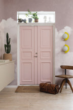 Fluffy Clouds wall mural by Rebel Walls in blush pink, framing a pink panelled door in a bright hallway