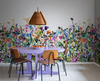 May Meadow mural by Rebel Walls, rainbow wildflower meadow in a dining room behind a lilac table with timber chairs