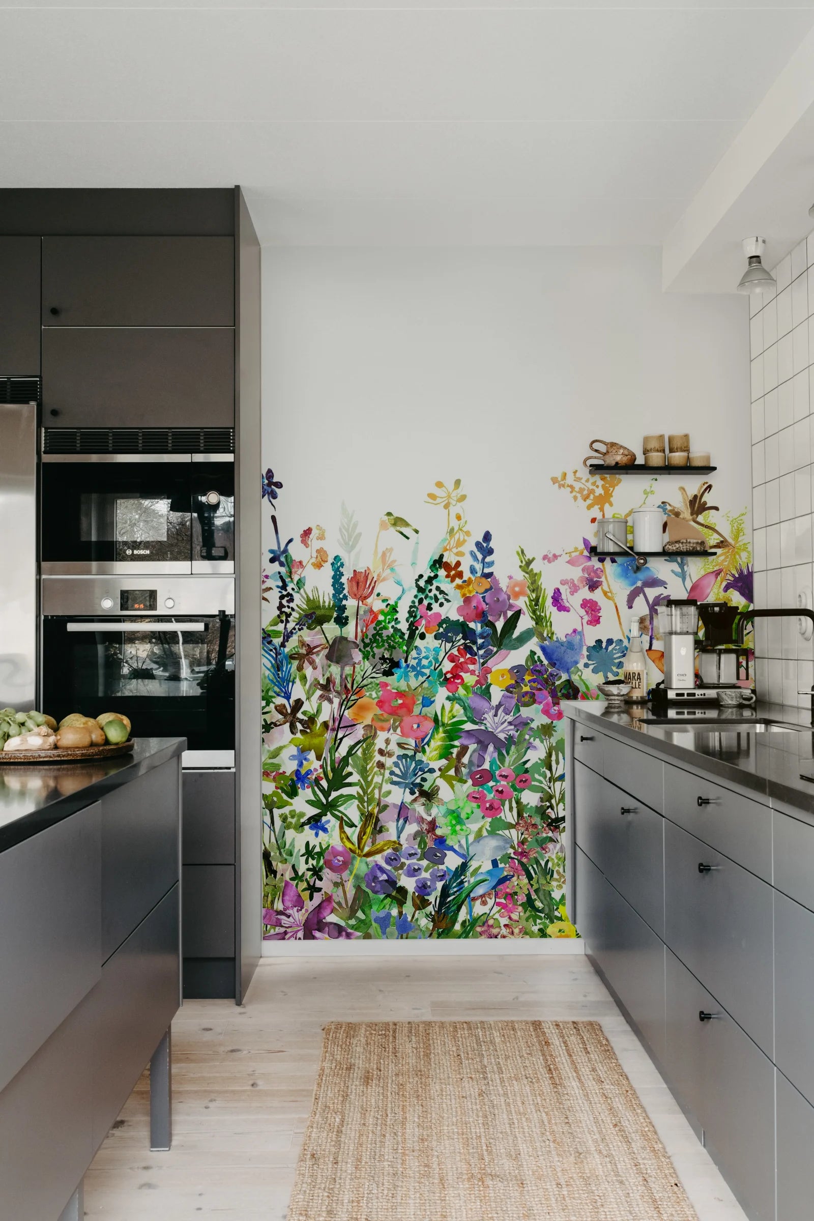 May Meadow mural by Rebel Walls, colourful watercolour wildflowers on a kitchen feature wall above dark grey cabinetry