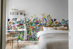 May Meadow mural by Rebel Walls, vivid wildflower meadow in a bedroom behind a linen bed with a corner desk and bookshelf