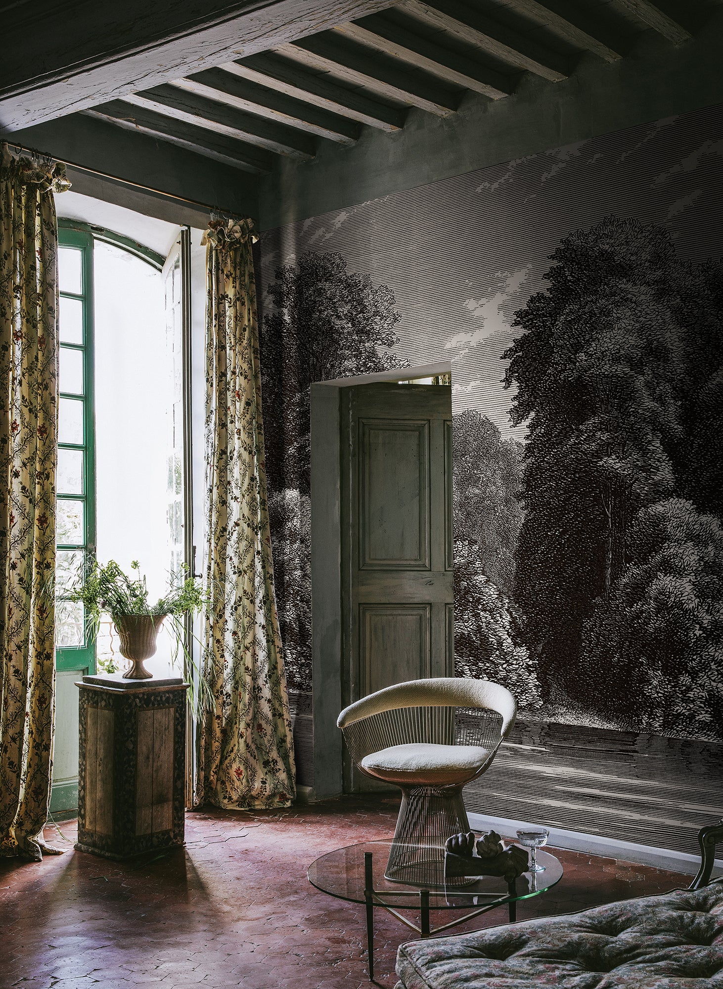 Spring Season wall mural by Rebel Walls, etched charcoal-grey woodland scene, styled in a rustic room with a velvet chair and tall floral drapes