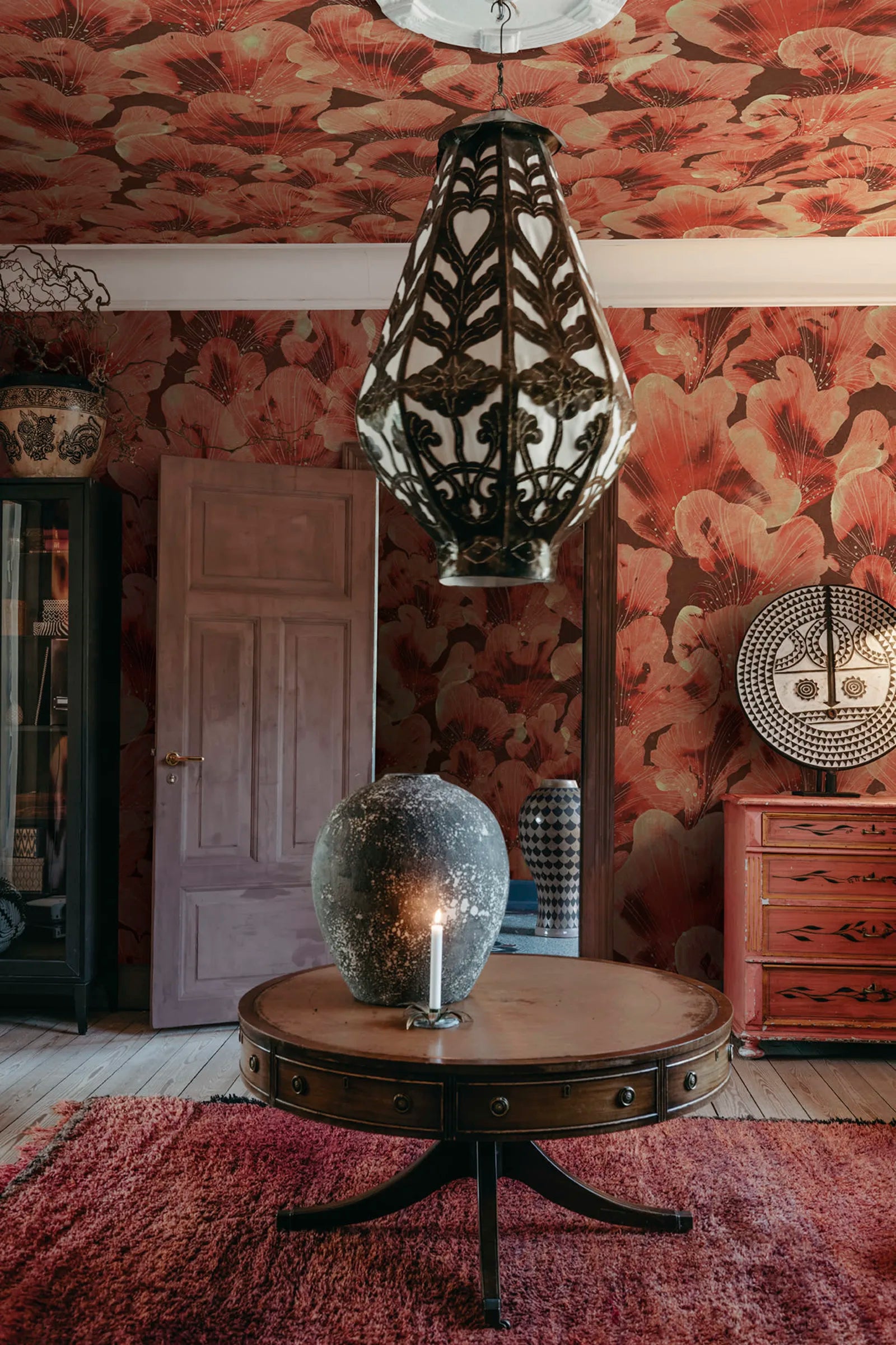 Corals wall mural by Rebel Walls in coral red on walls and ceiling, with drum table and ornate pendant lamp