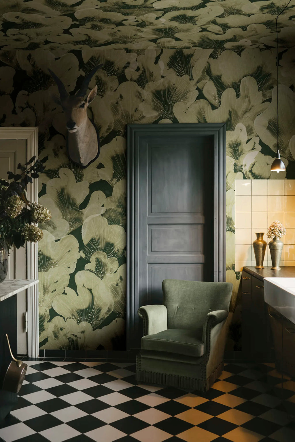 Corals wall mural by Rebel Walls in green, behind a grey door and velvet armchair with mounted antelope head
