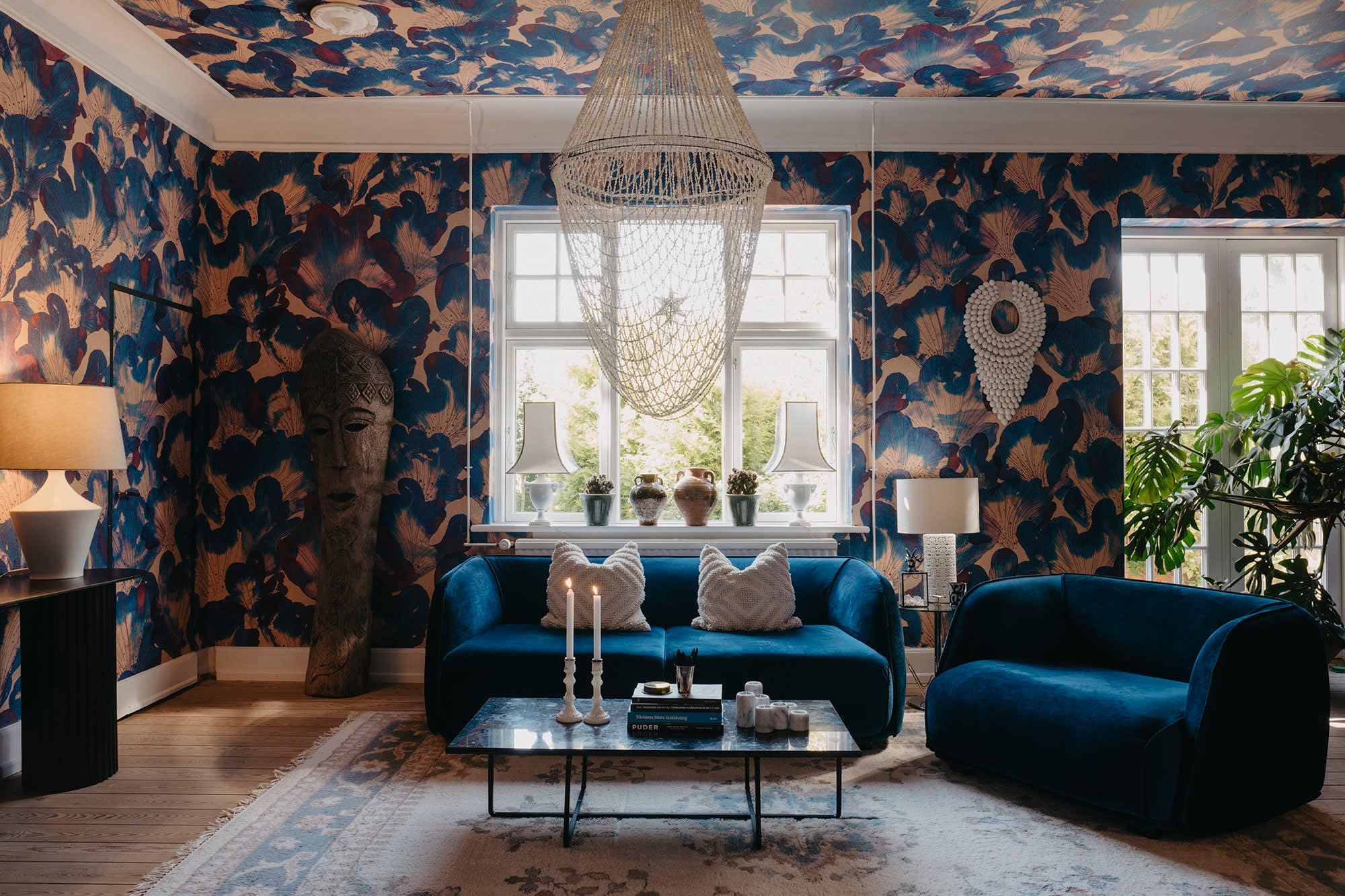 Corals wall mural by Rebel Walls in blue and magenta, wrapping a living room with blue velvet sofas and beaded chandelier