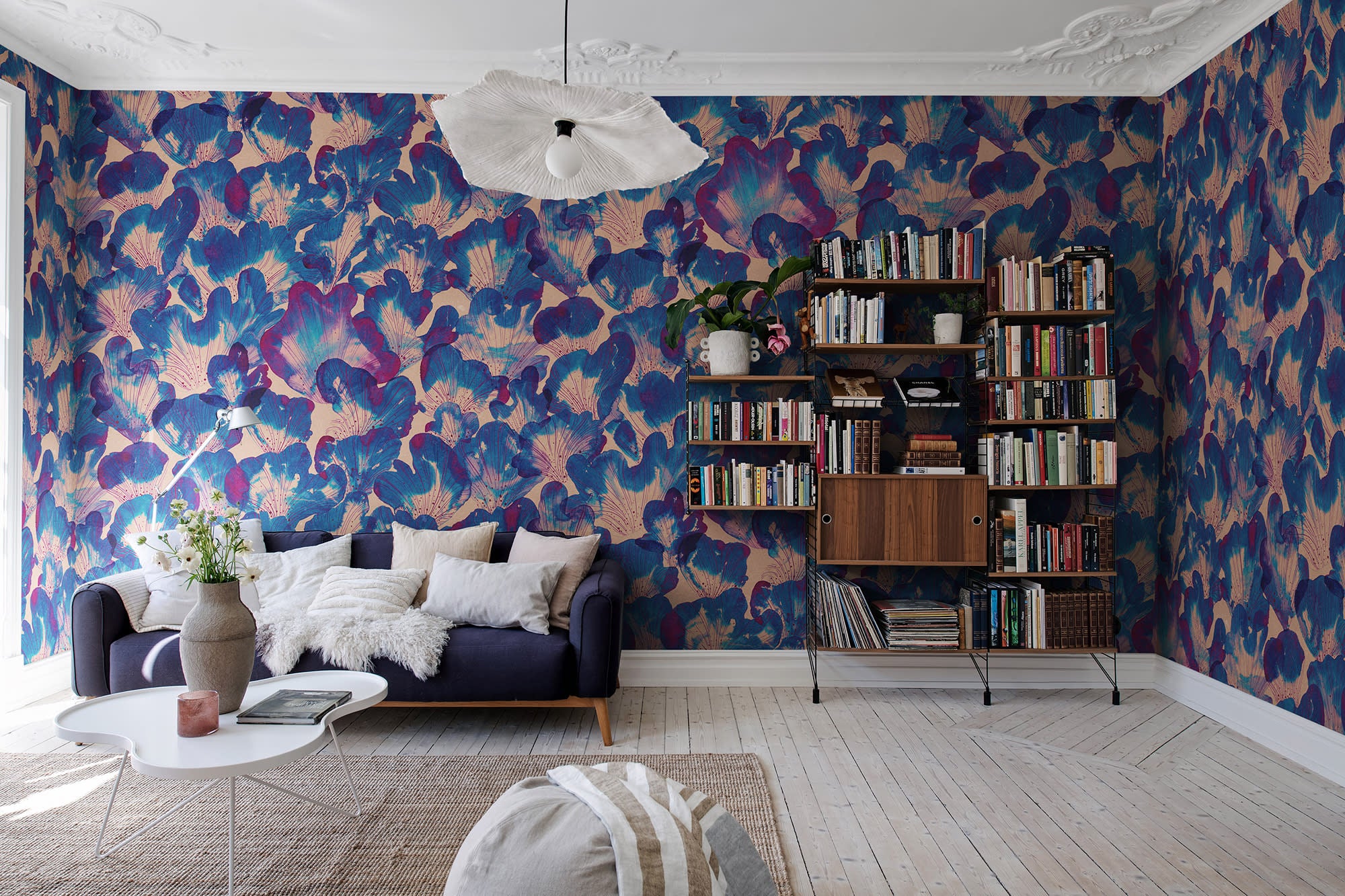 Corals wall mural by Rebel Walls in blue and magenta, in a lounge with navy sofa and timber bookshelf