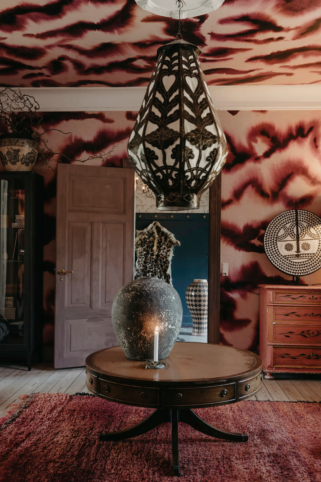 Guppy wall mural by Rebel Walls in burgundy and blush swirls covering walls and ceiling of a styled room with drum table