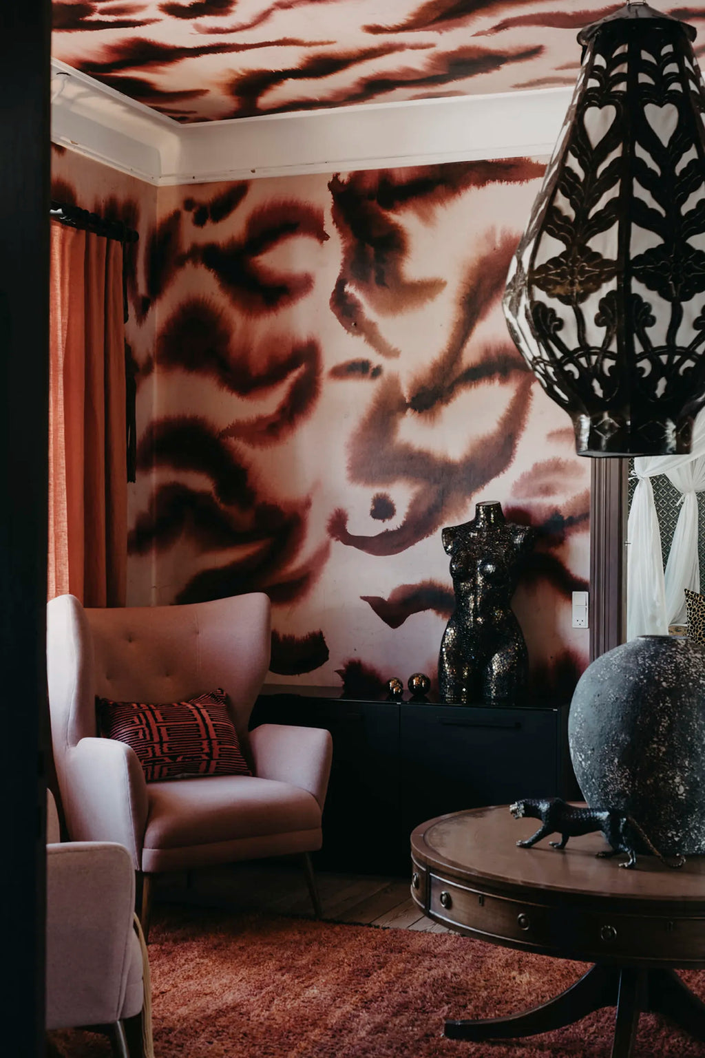 Guppy wall mural by Rebel Walls in burgundy and pink swirls, styled with a pink armchair and ornate pendant lamp