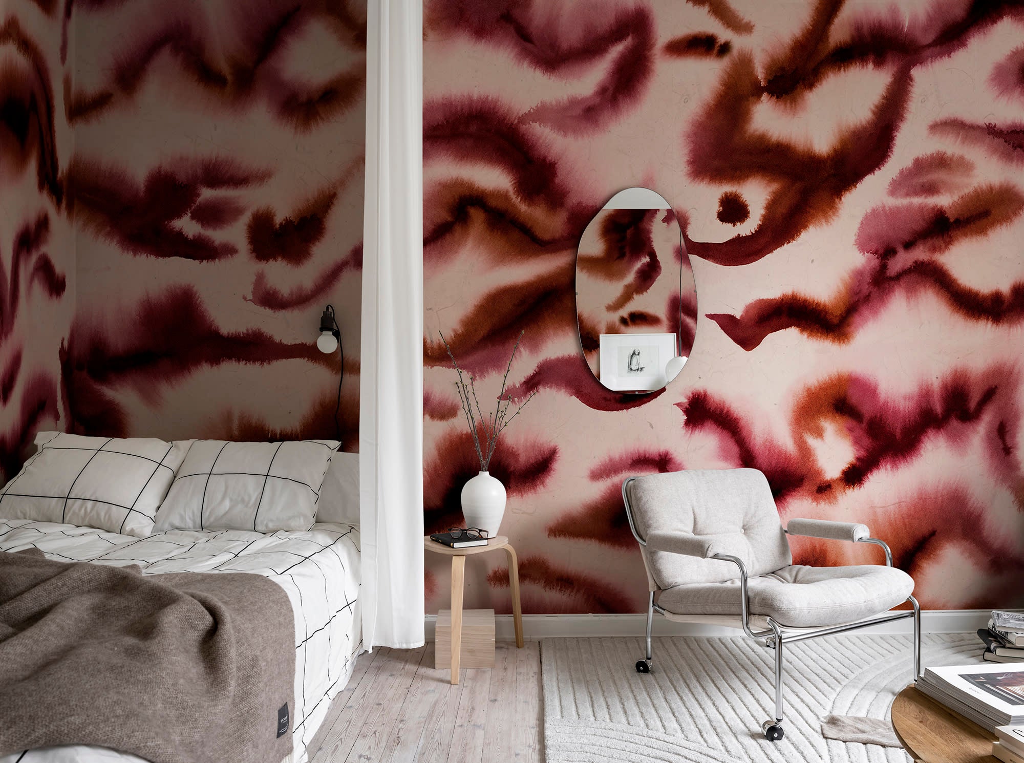 Guppy wall mural by Rebel Walls in burgundy and blush swirls, in a bedroom with oval mirror and grey armchair