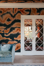 Guppy wall mural by Rebel Walls in orange and navy swirls, beside white panelled doors with a blue daybed