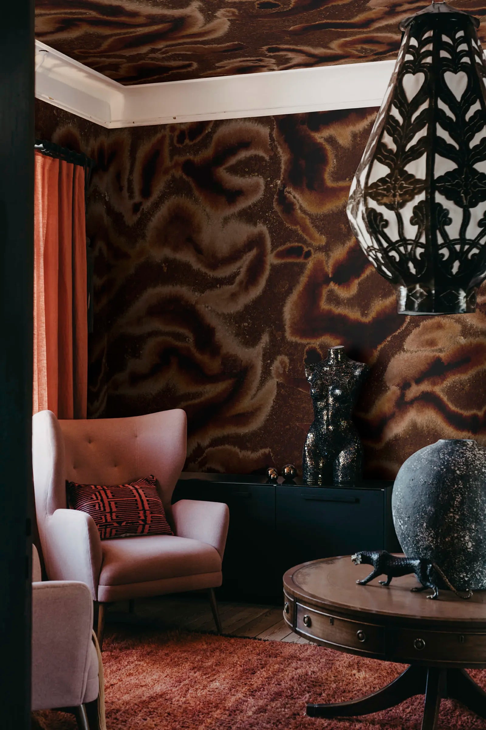 Guppy wall mural by Rebel Walls in dark brown swirls, styled in a corner with pink armchair and rust curtain